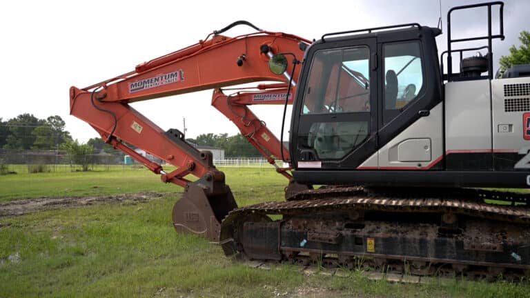 Orange hydraulic excavator on a grassy construction site, with a tracked undercarriage and front cabin